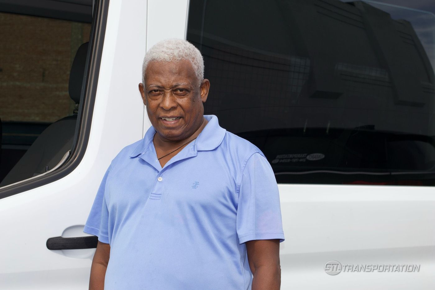 A veteran STL Transportation driver standing beside a fleet van